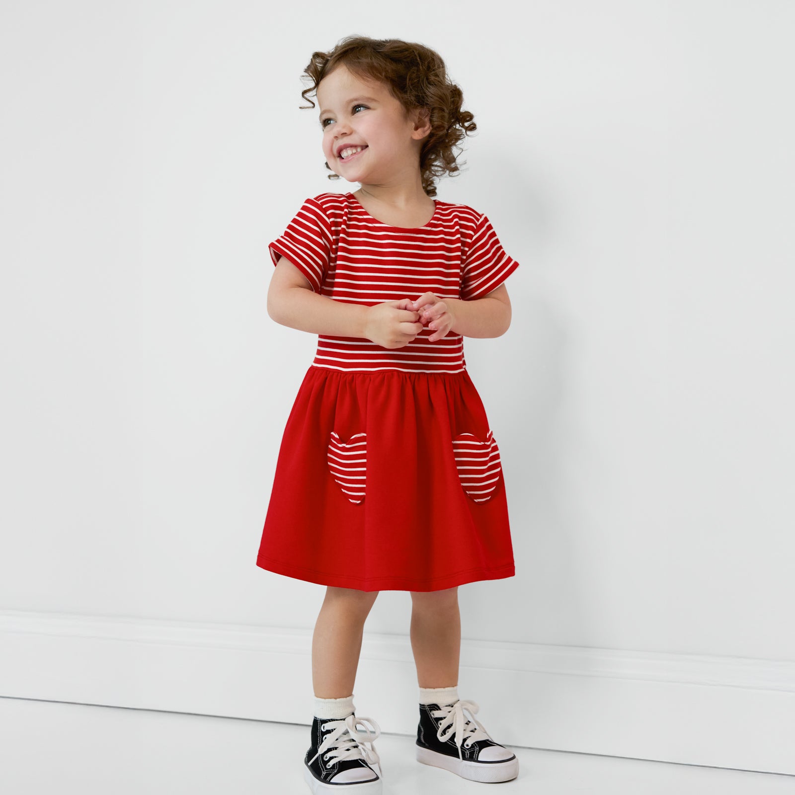 Child looking to the side and smiling wearing a Candy Red Patch Pocket Dress with Bloomer