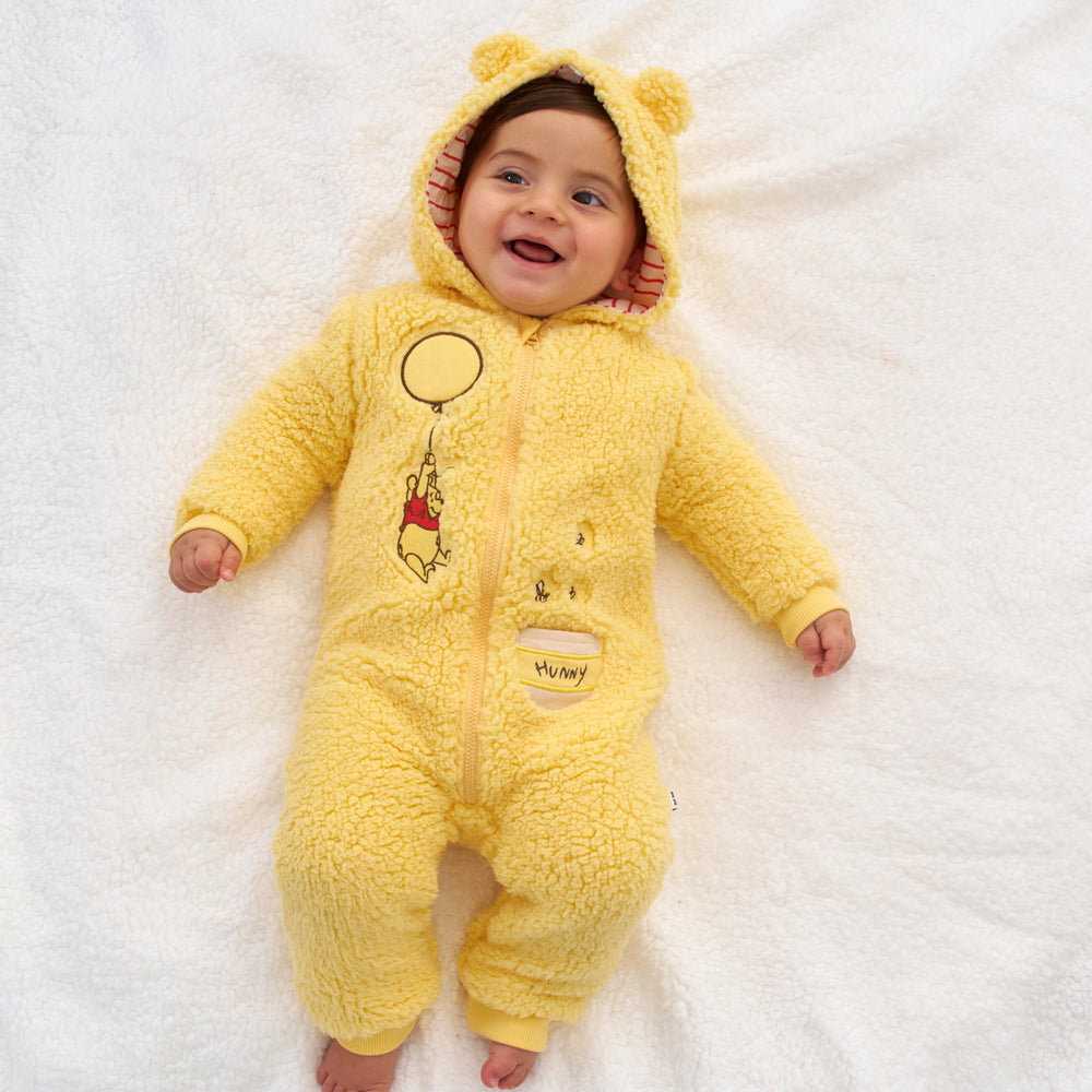 Click to see full screen - Child laying on a blanket wearing a Disney Winnie the Pooh sherpa romper with the hood up