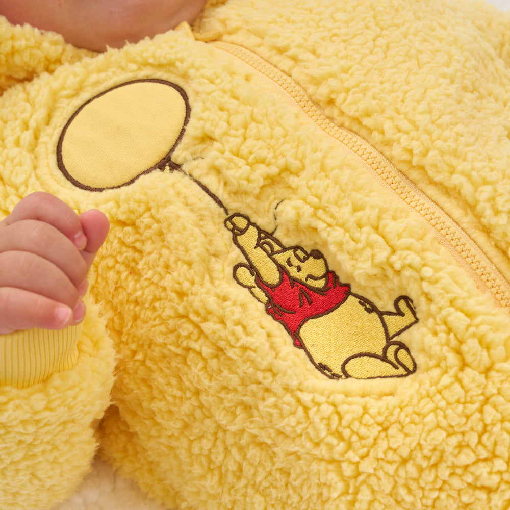 Click to see full screen - Close up image of a child wearing a Disney Winnie the Pooh sherpa romper detailing the embroidered image of Winnie the Pooh