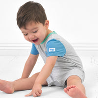 Alternate image of a child sitting on the ground wearing a Bluey graphic pocket shorty romper