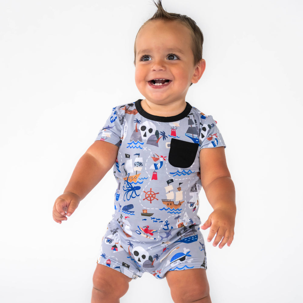 Baby standing while wearing the Pirate's Map Pocket Shorty Romper