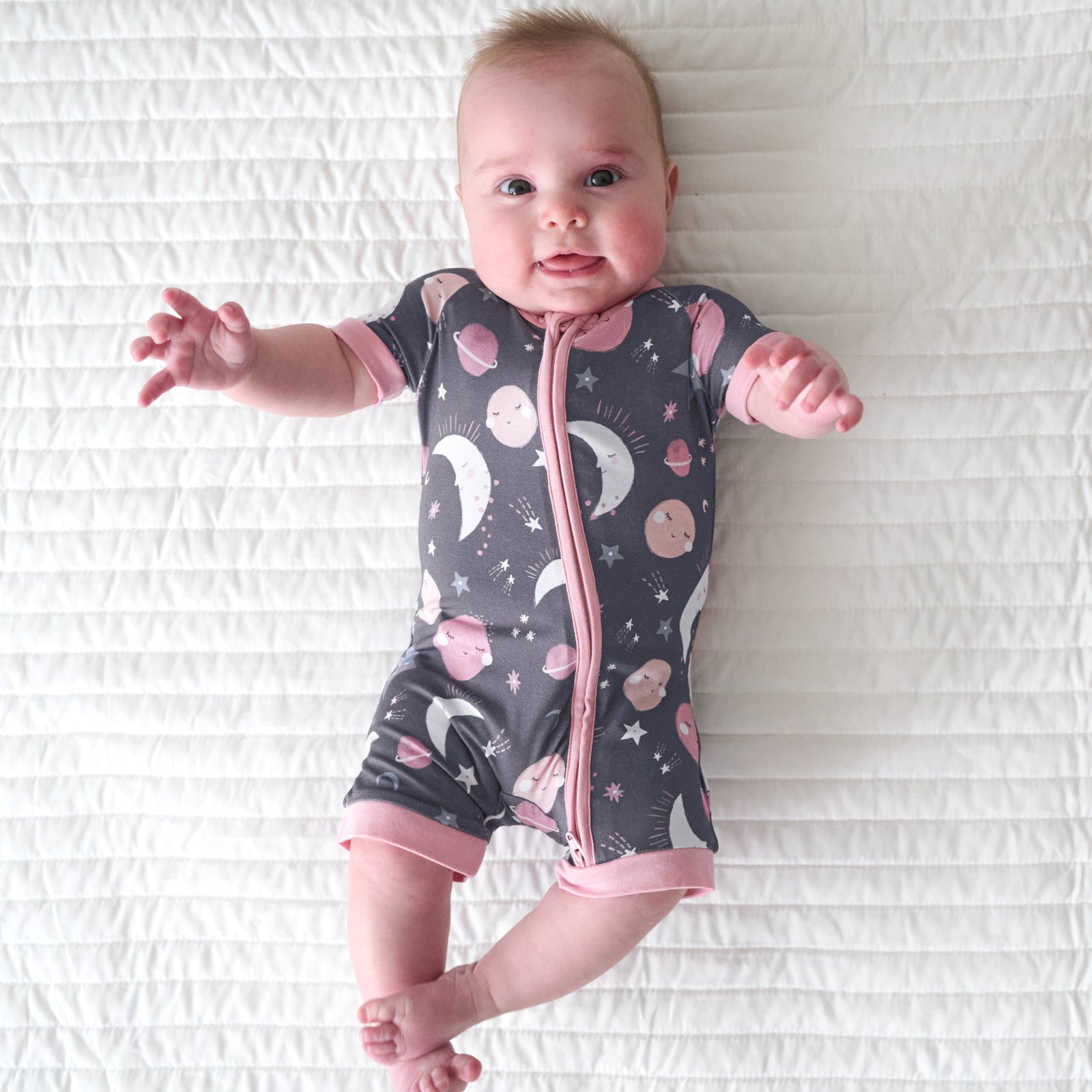 Child laying on a bed wearing a Pink to the Moon and Back shorty zippy