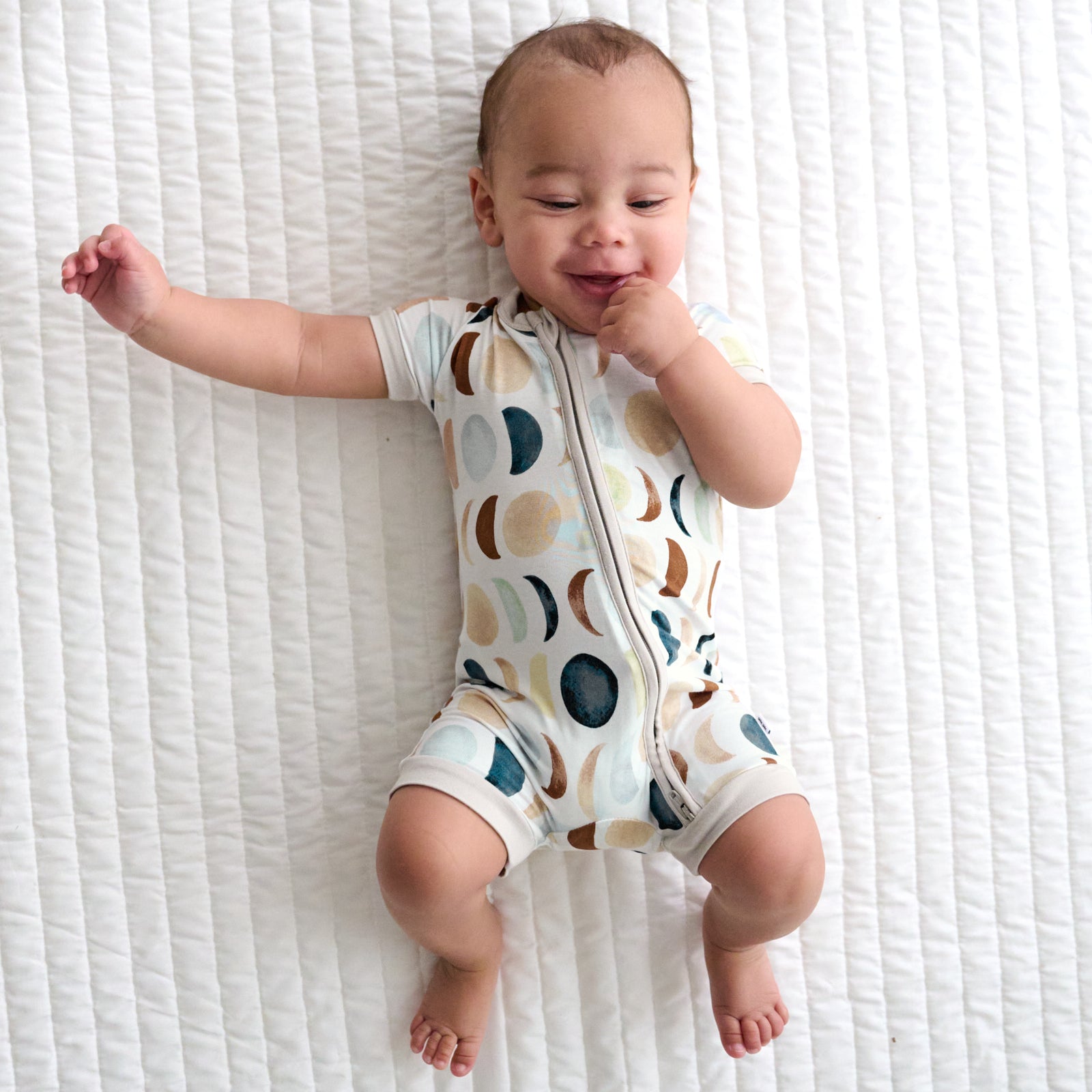 Child laying on a bed wearing a Luna Neutral shorty zippy