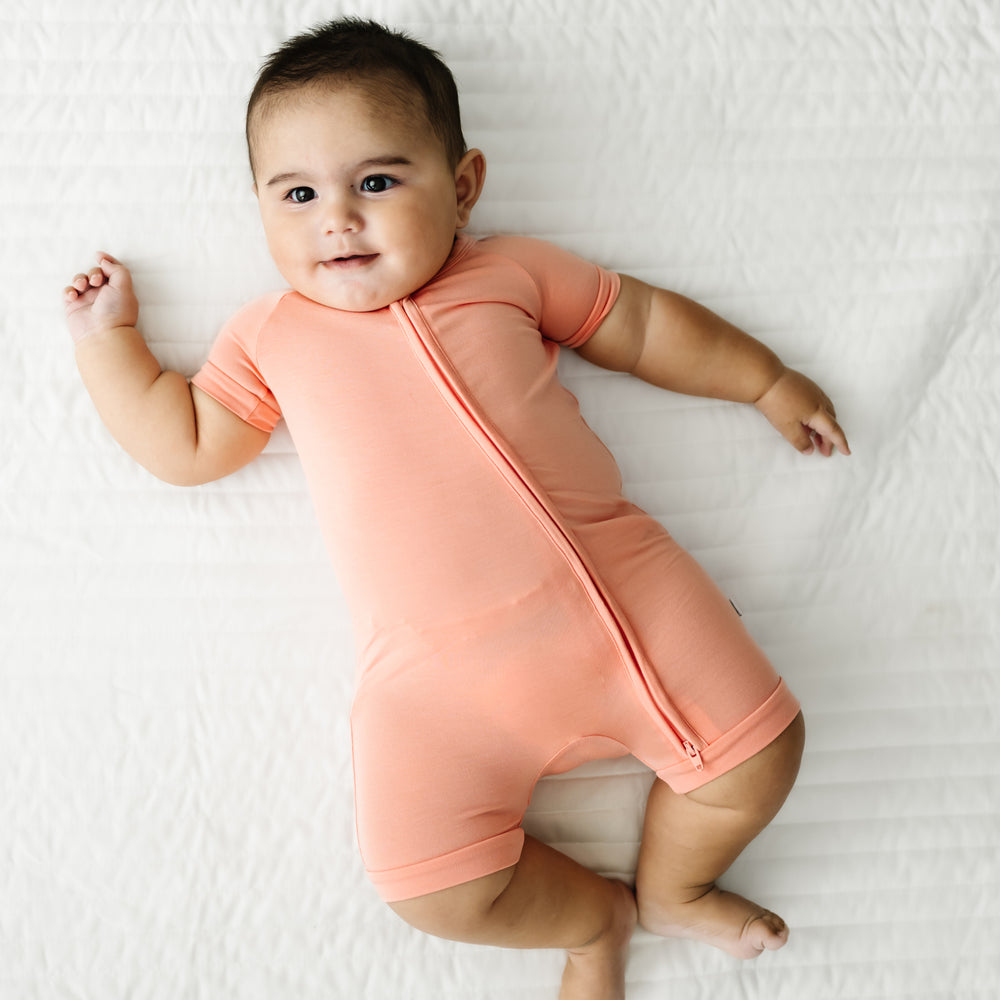 Child laying on a bed wearing a Peach shorty zippy