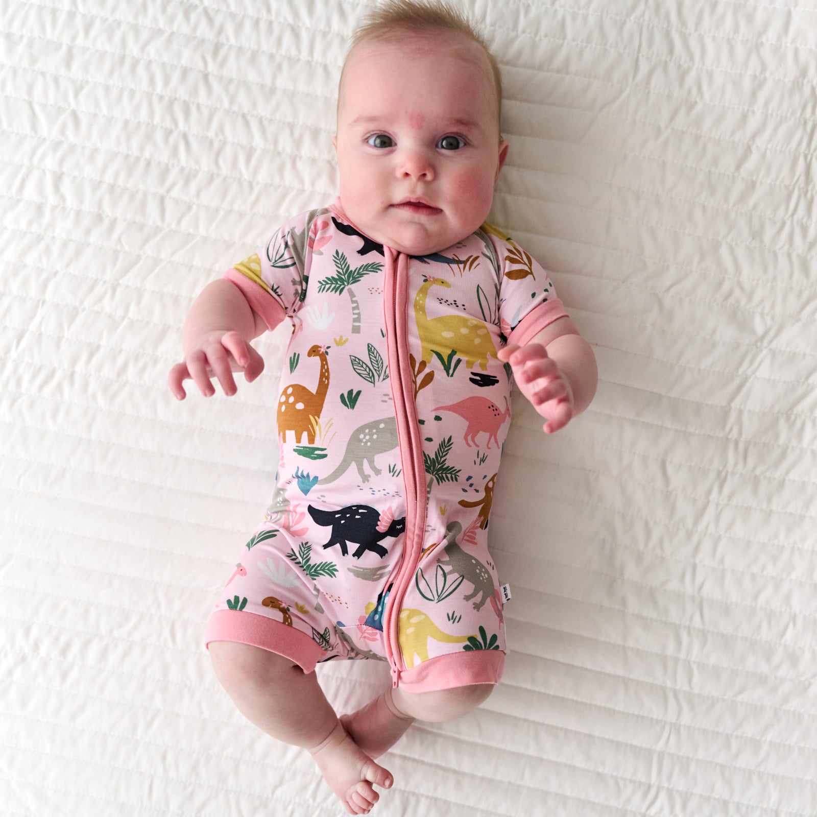 Child laying on a bed wearing a Pink Jurassic Jungle Shorty Zippy