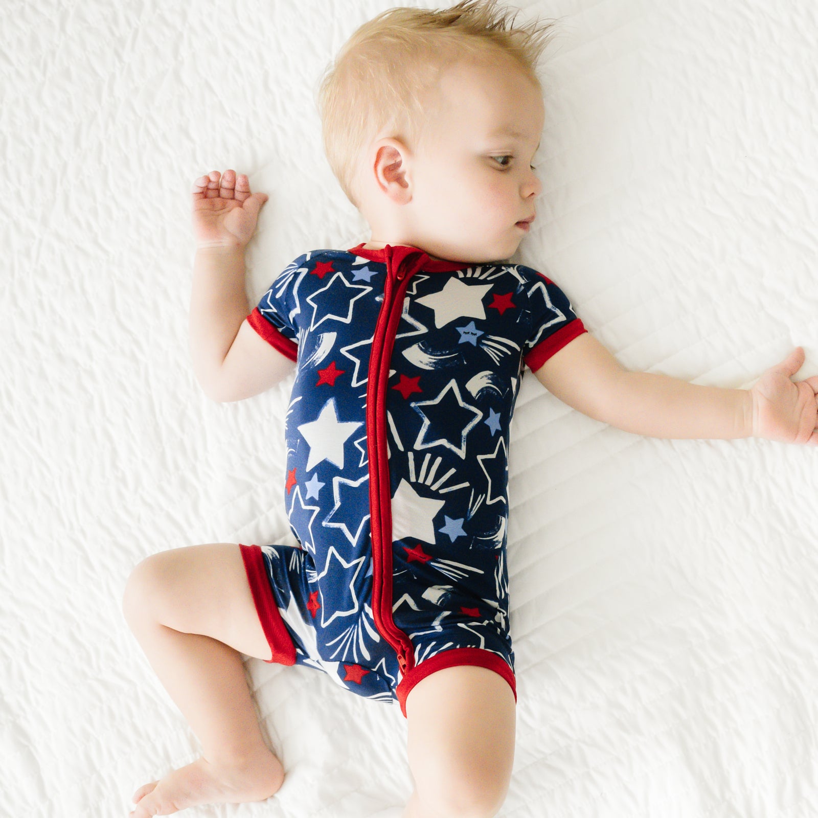 Child laying on a bed wearing a Star Spangled shorty zippy