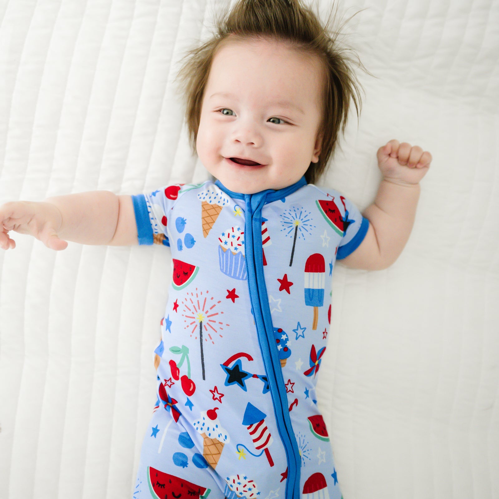 Close up image of a child laying on a bed wearing a Stars, Stripes, and Sweets shorty zippy