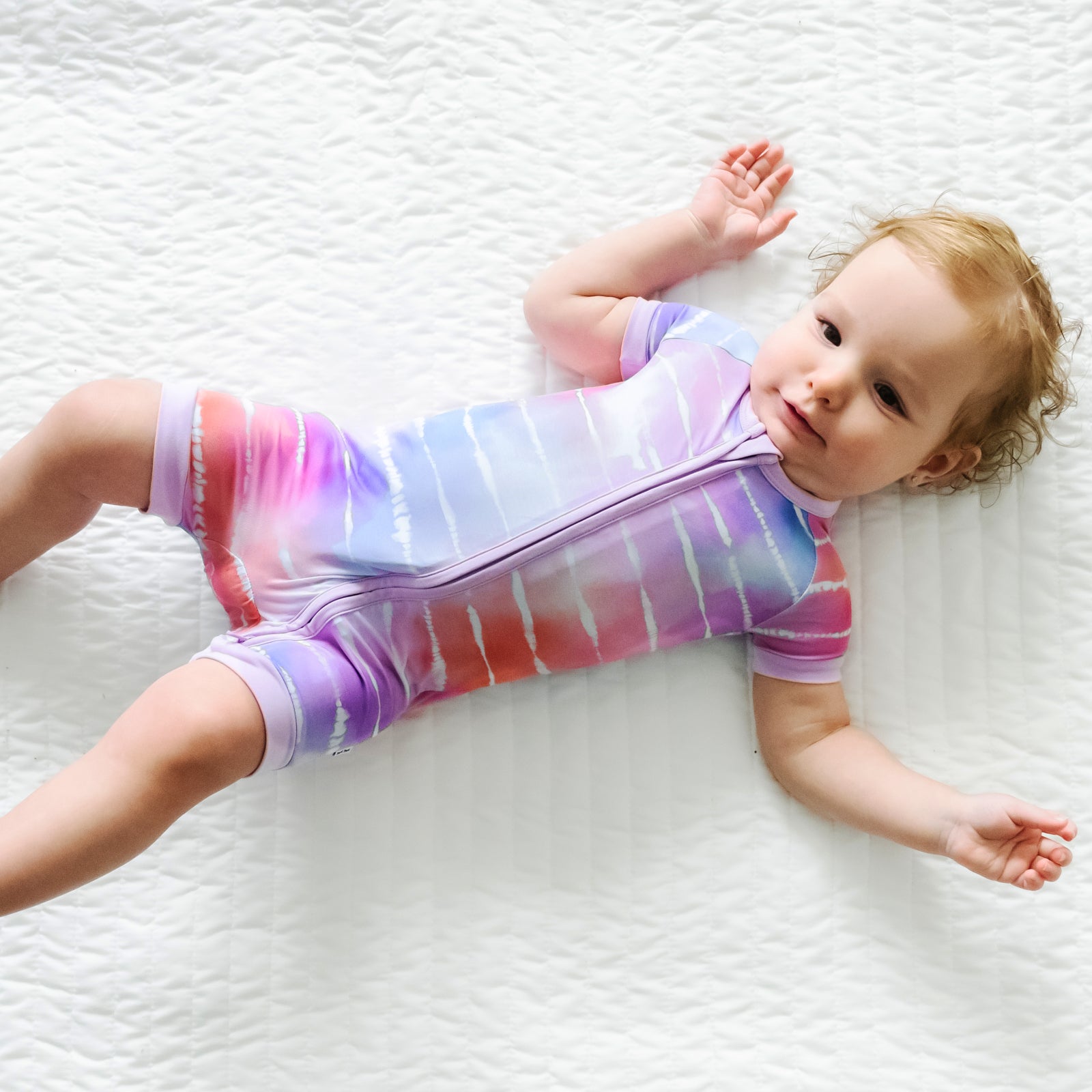 Child laying on a blanket wearing a Pastel Tie Dye Dreams shorty zippy