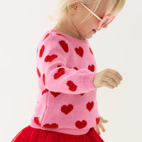 Close up side view image of a child wearing a Hearts knit sweater