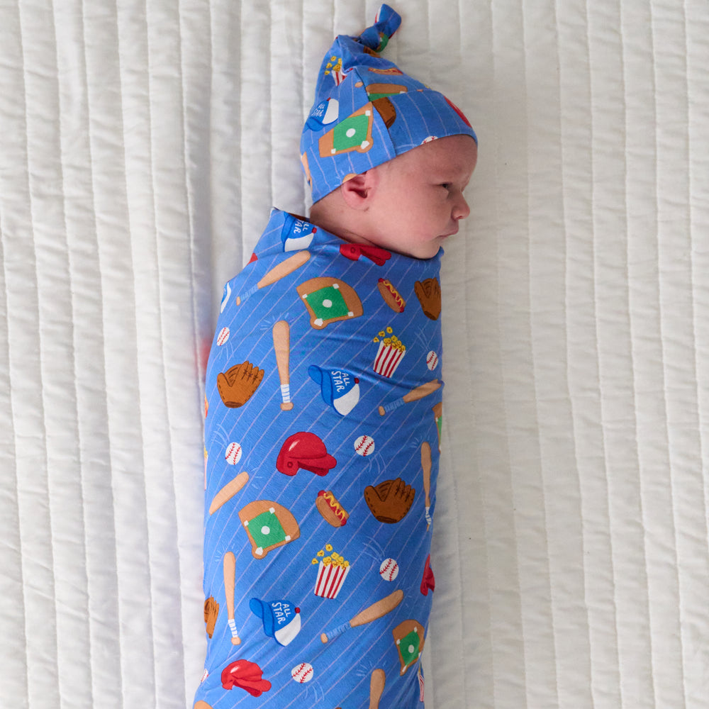 Child laying on a bed swaddled in a Blue All Stars swaddle and hat set