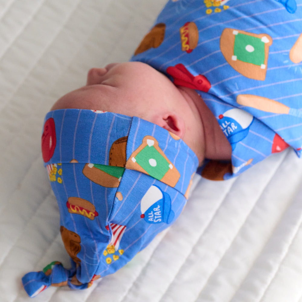 Close up image of a child swaddled in a Blue All Stars swaddle and hat set showing off the knotted hat