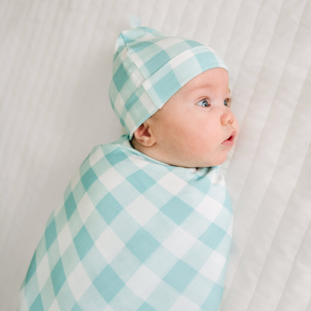 Click to see full screen - Close up image of a child swaddled in a Aqua Gingham swaddle and hat set