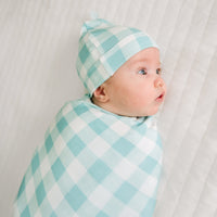 Close up image of a child swaddled in a Aqua Gingham swaddle and hat set