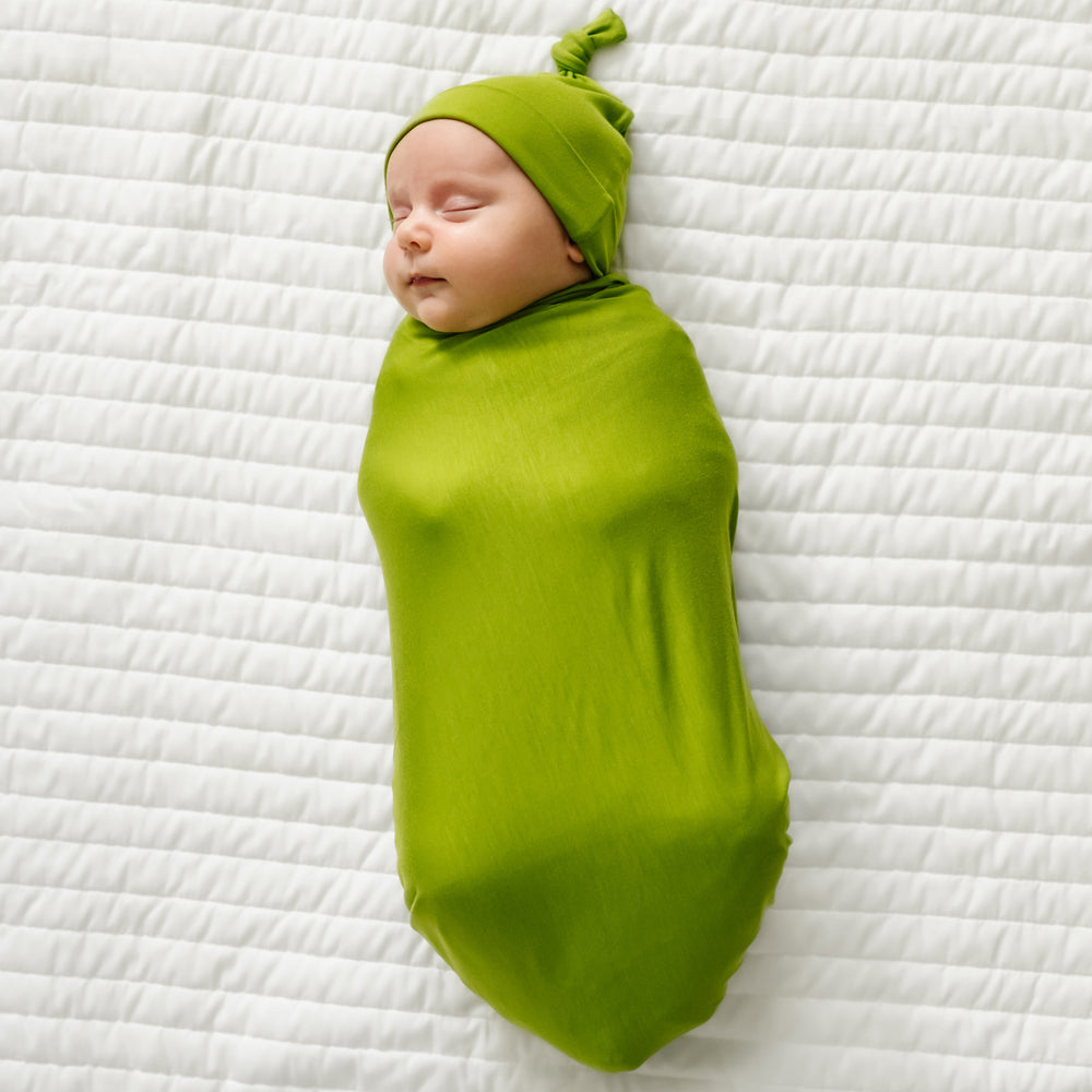 Child swaddled on a bed wearing an Avocado swaddle and hat set