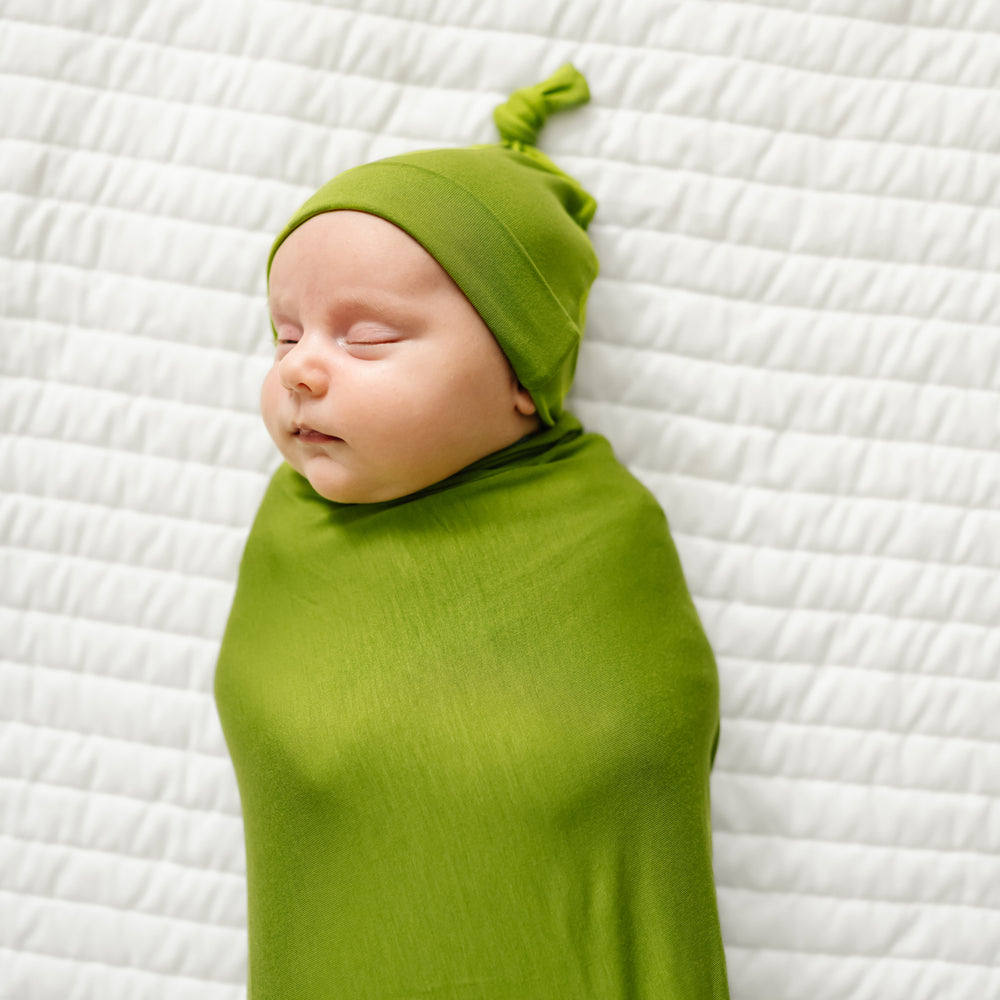 Alternate image of a child swaddled on a bed wearing an Avocado swaddle and hat set