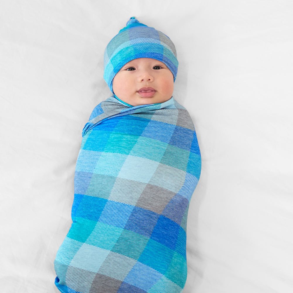 Alternate image of a child swaddled on a bed in an Arctic Plaid swaddle and hat set