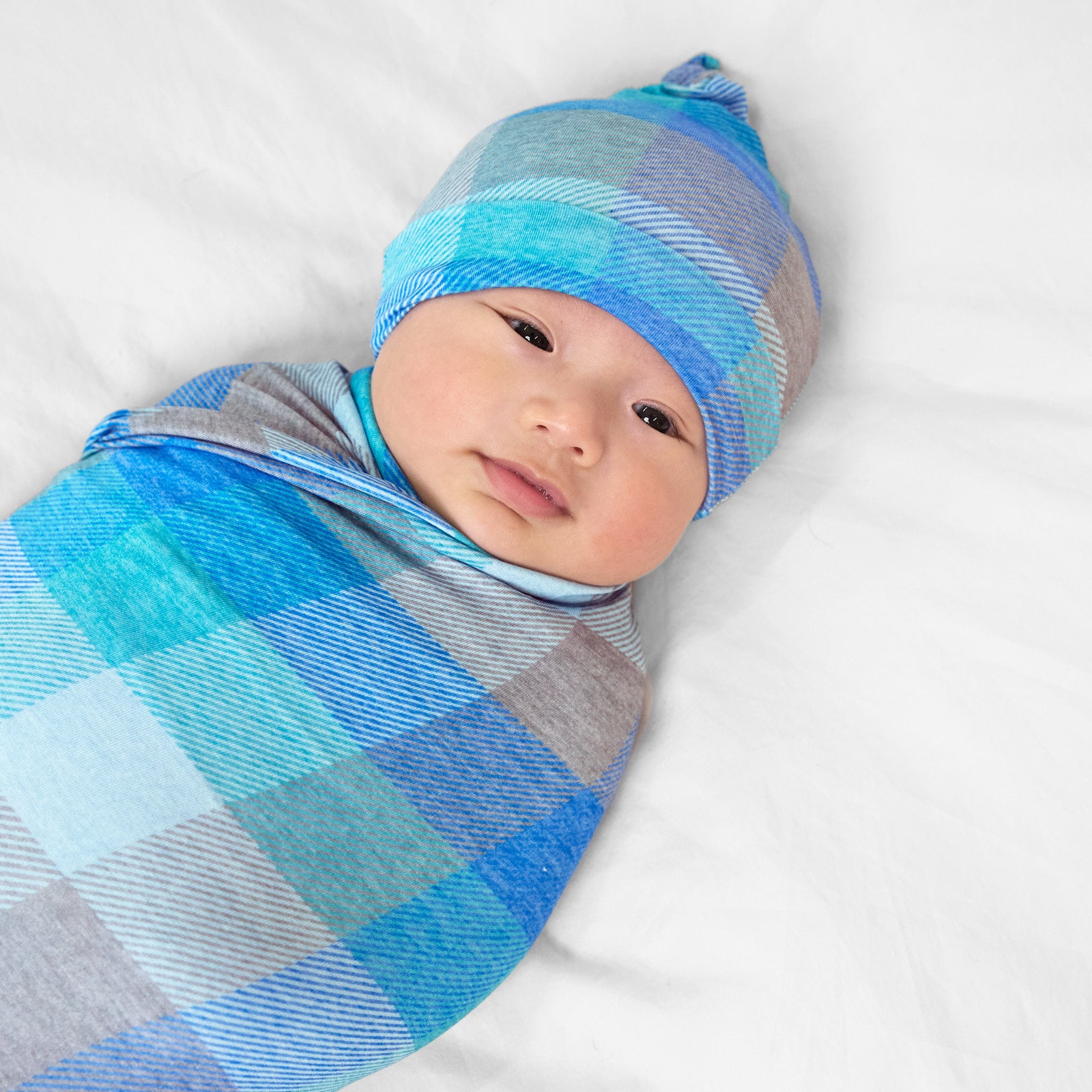 Close up image of a child swaddled on a bed in an Arctic Plaid swaddle and hat set