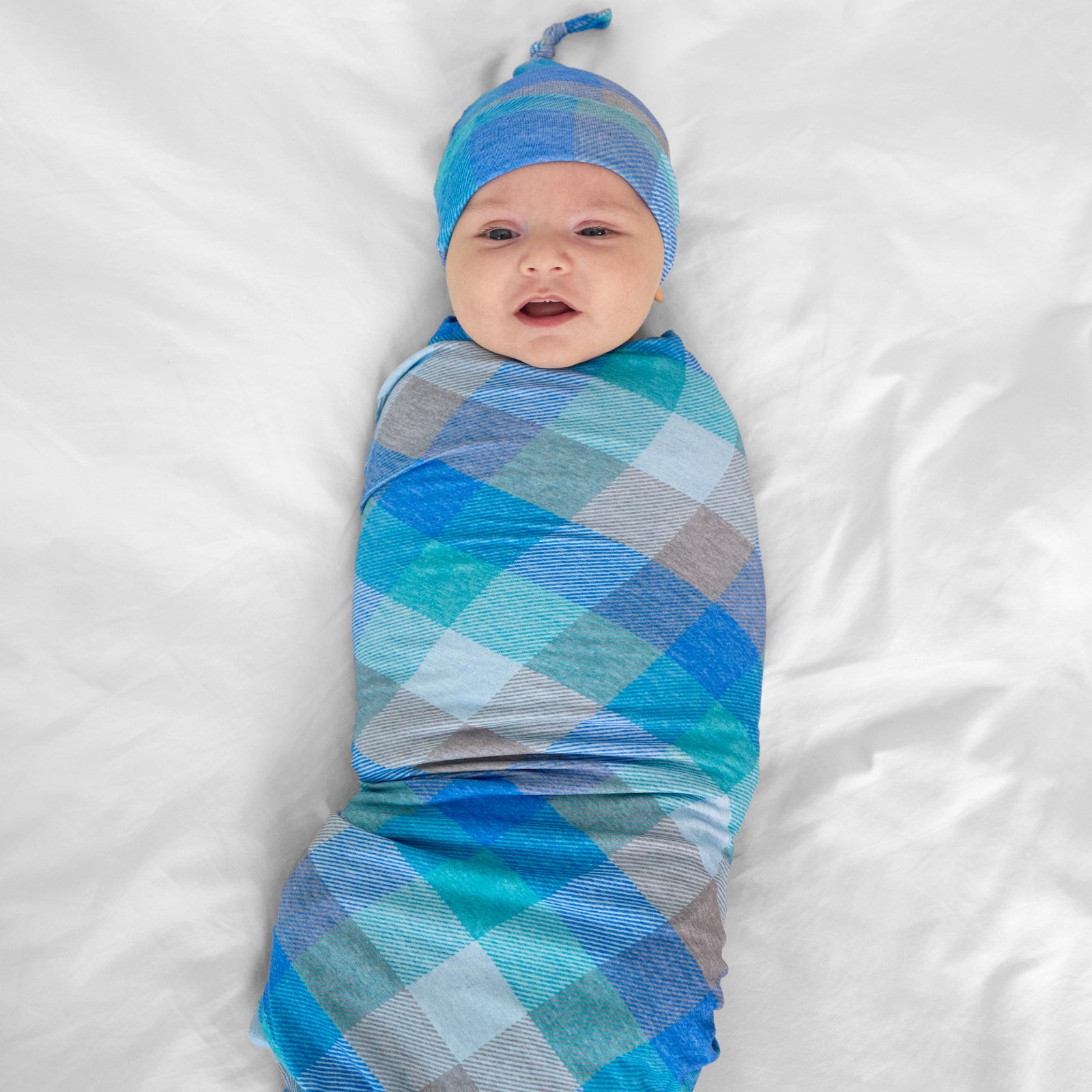 Child swaddled on a bed in an Arctic Plaid swaddle and hat set