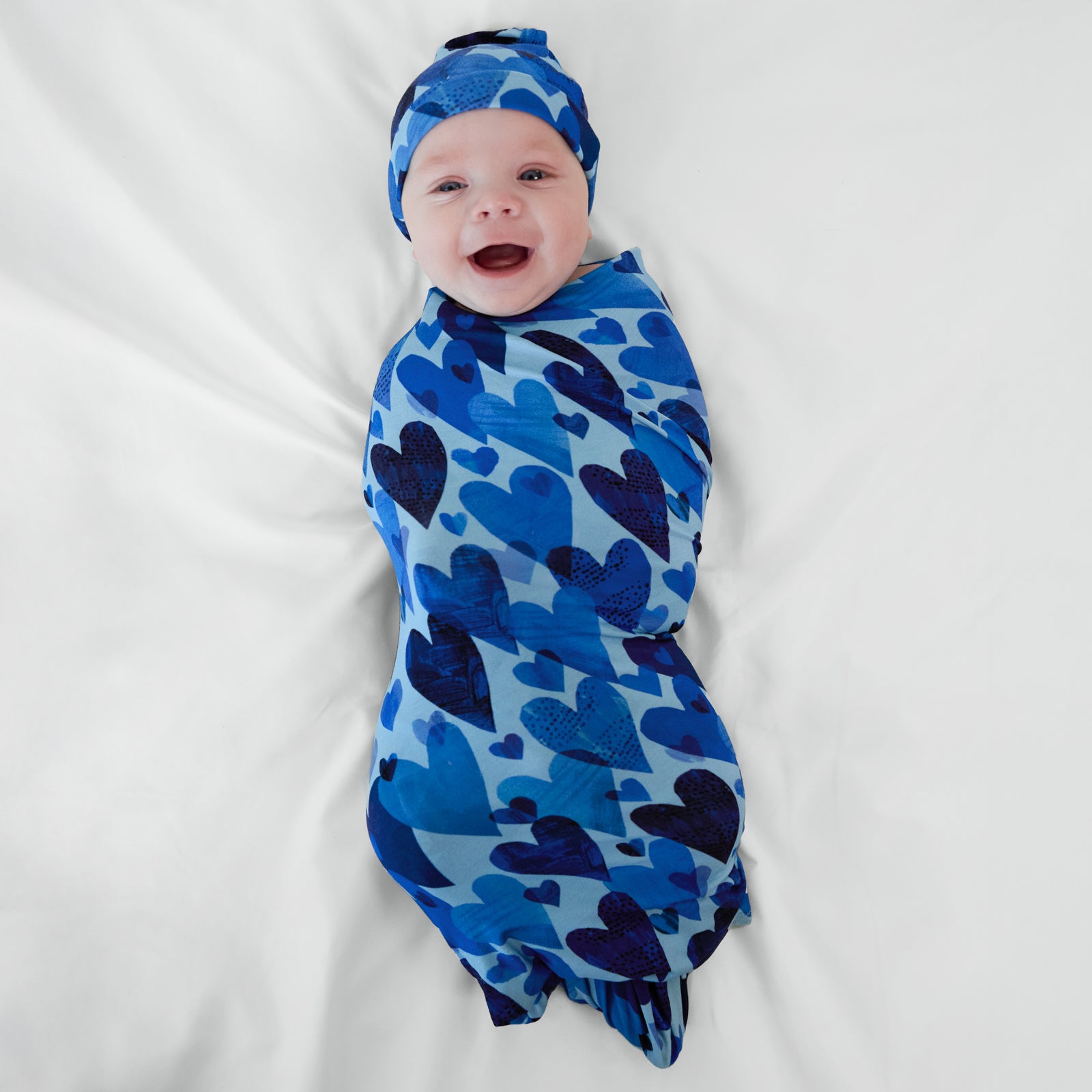 Infant in Blue Hearts & Crafts swaddle and hat set.