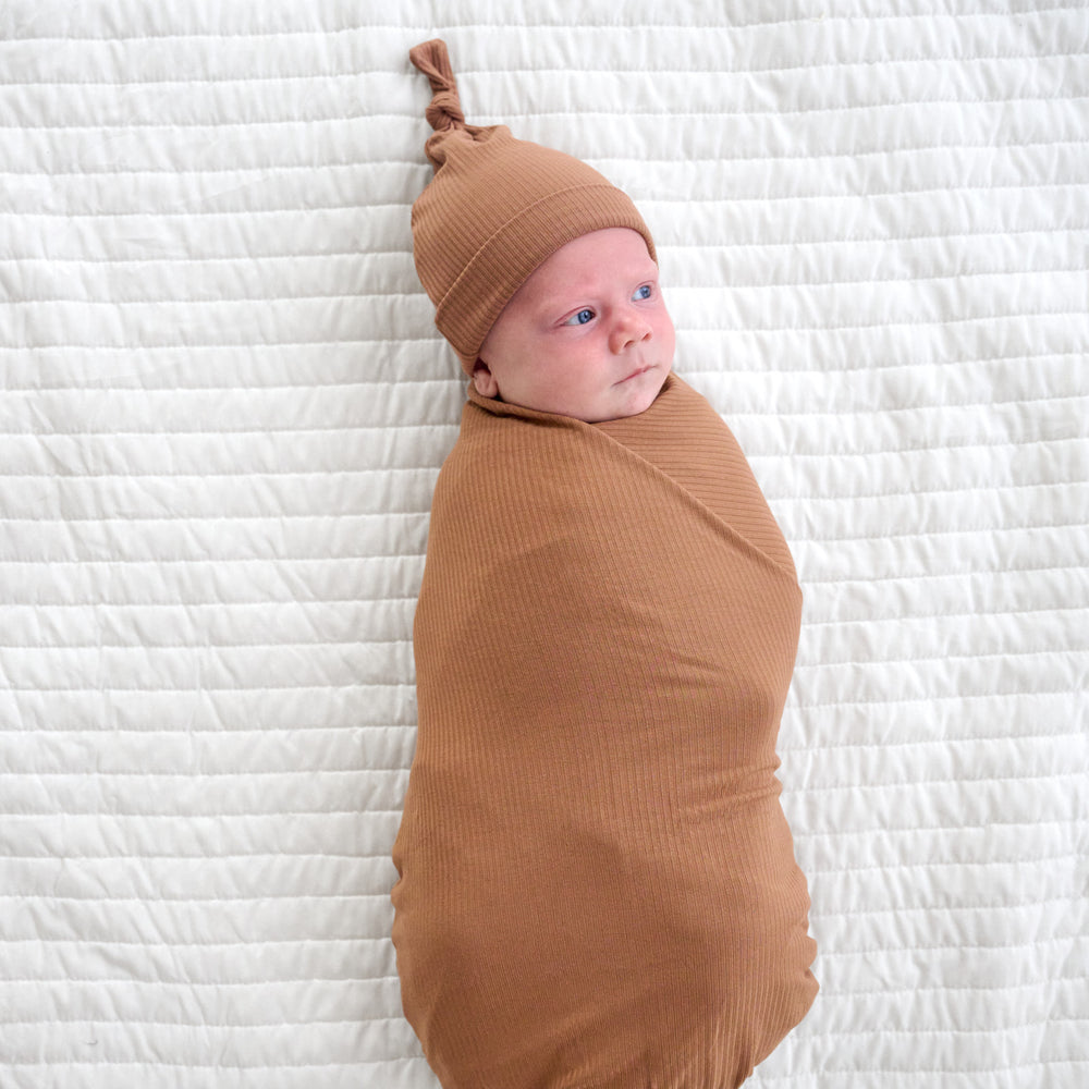 Top view image of baby laying down while wrapped in the Caramel Ribbed Swaddle & Hat Set