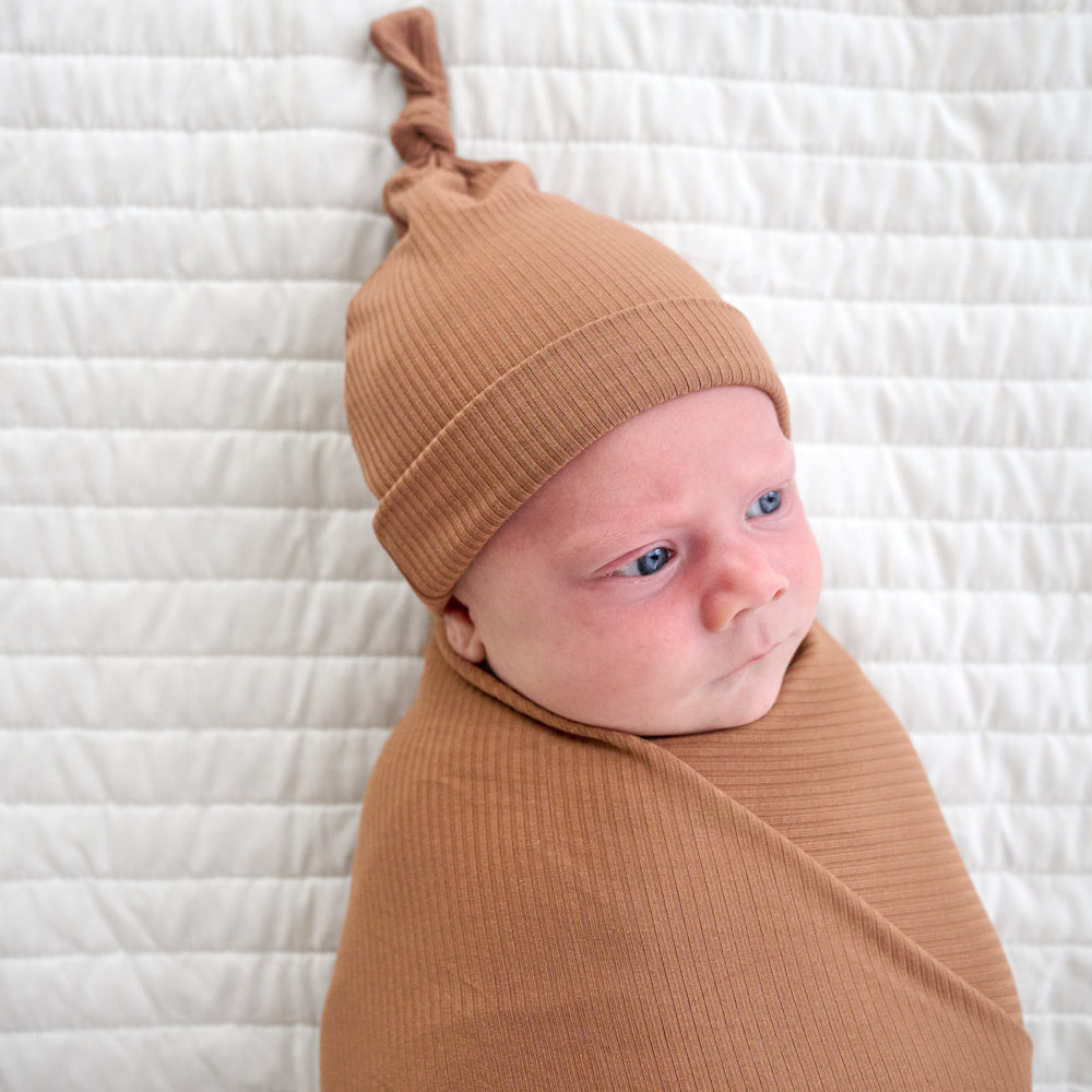 Close up image of baby laying down while wearing the hat in the Caramel Ribbed Swaddle & Hat Set