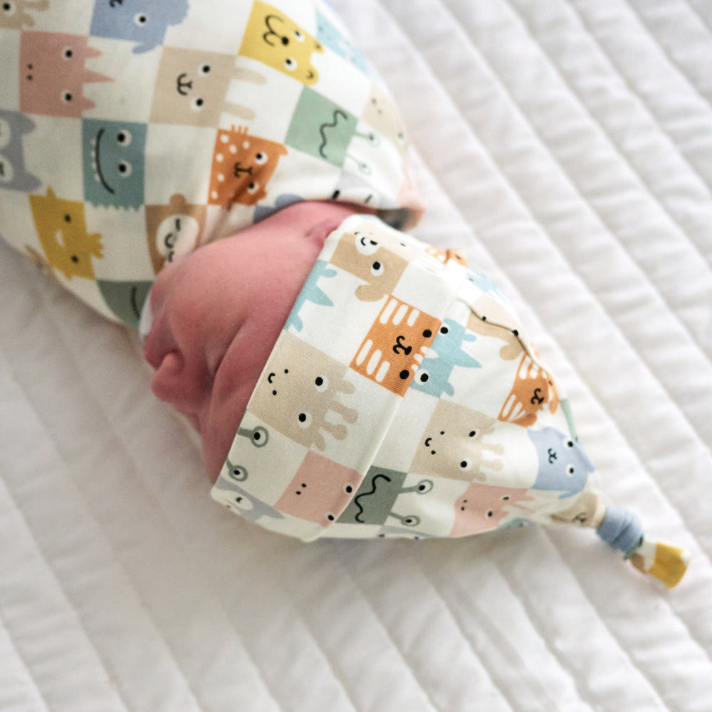Close up image of an infant swaddled in a Check Mates swaddle and hat set