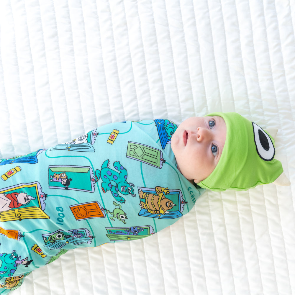 Close up top view image of baby laying down while in the Disney Monsters, Inc. Scream Team Swaddle & Hat Set