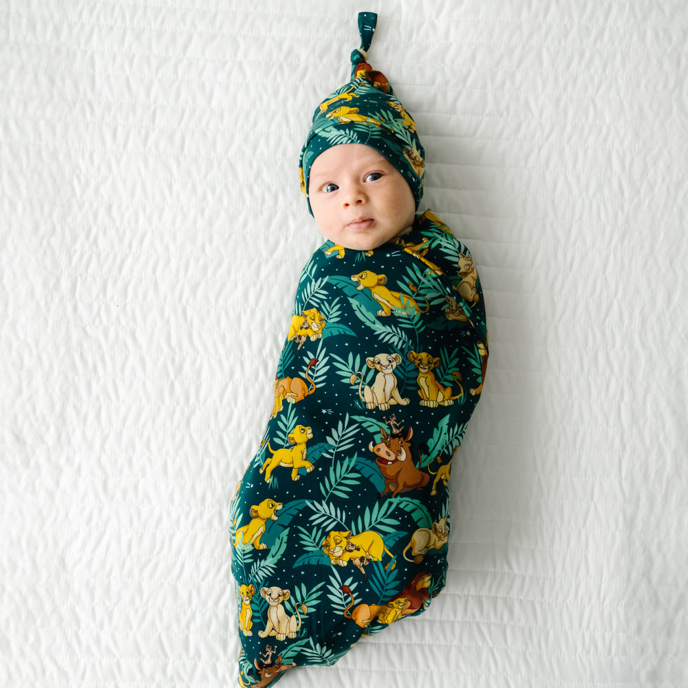 Child laying on a bed swaddled in a Disney Simba's Sky swaddle and hat set