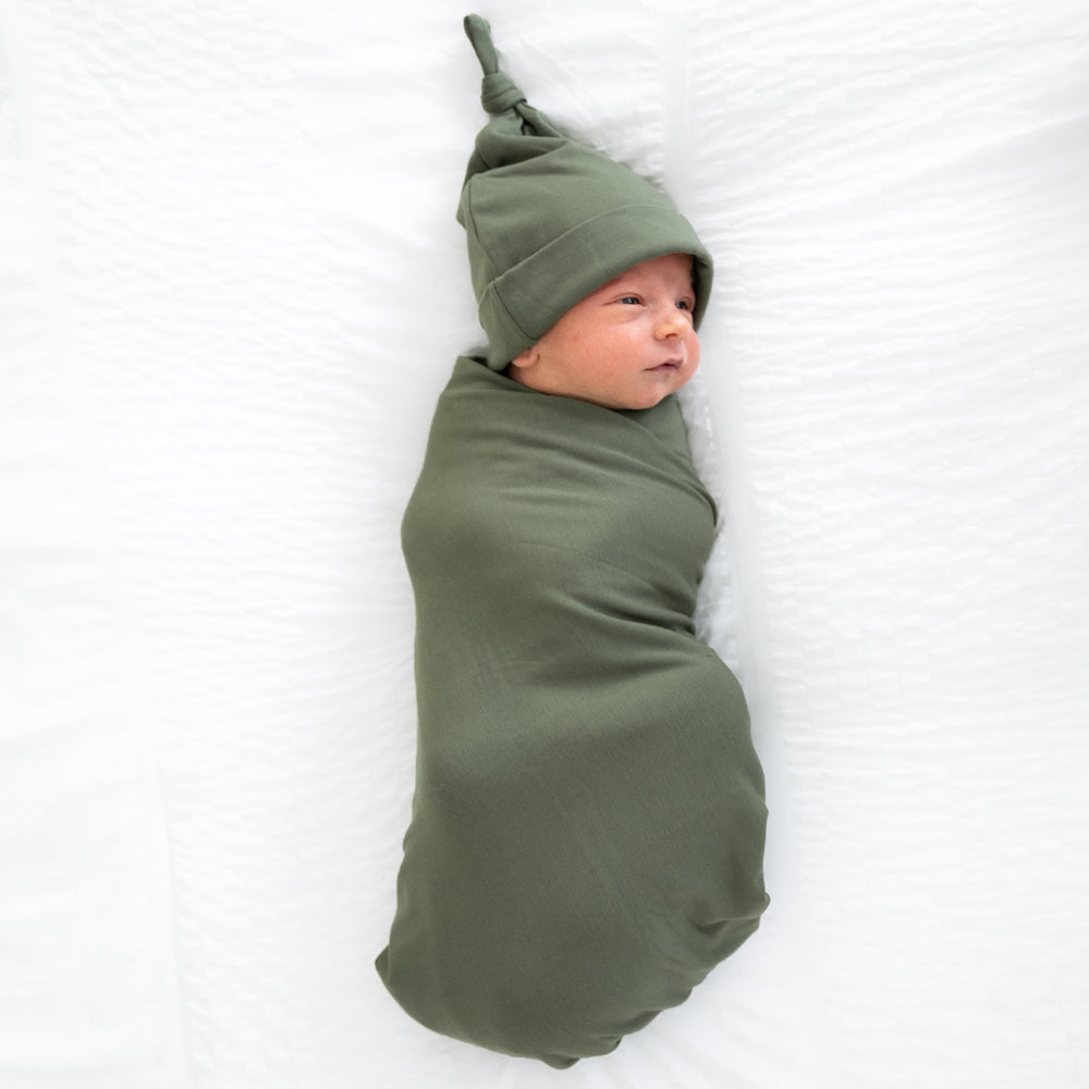 Child swaddled in a Cozy Olive swaddle and hat set