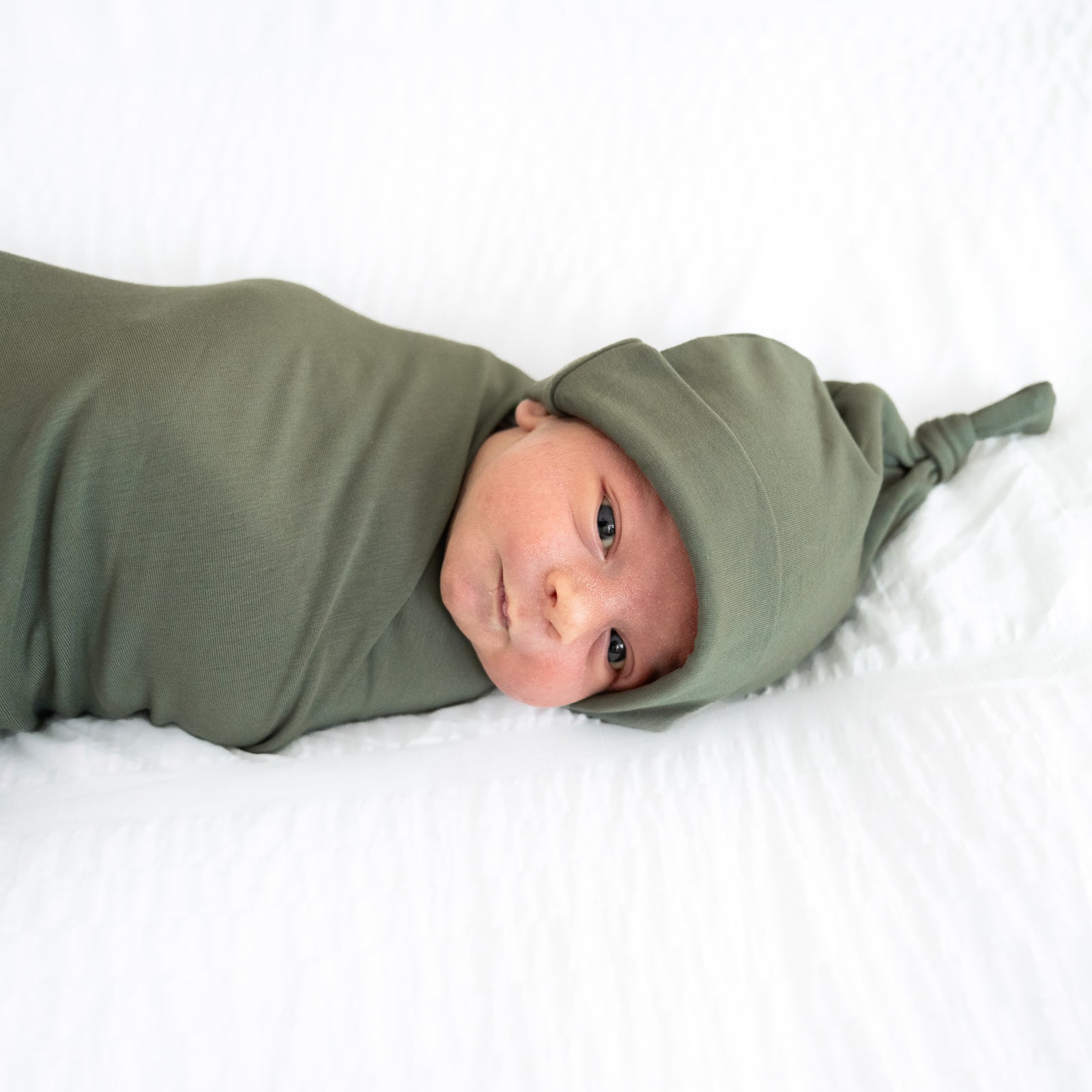 Close up image of a child swaddled in a Cozy Olive swaddle and hat set