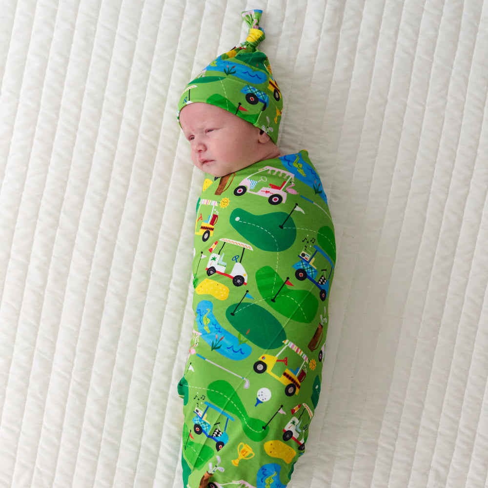 Infant swaddled in a Fairway Fun swaddle and hat set