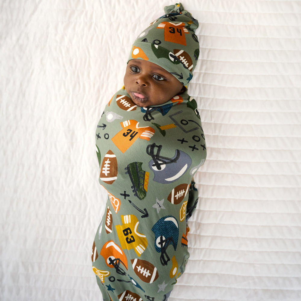 Top view image of baby laying down in the Touchdown Time Swaddle & Hat Set