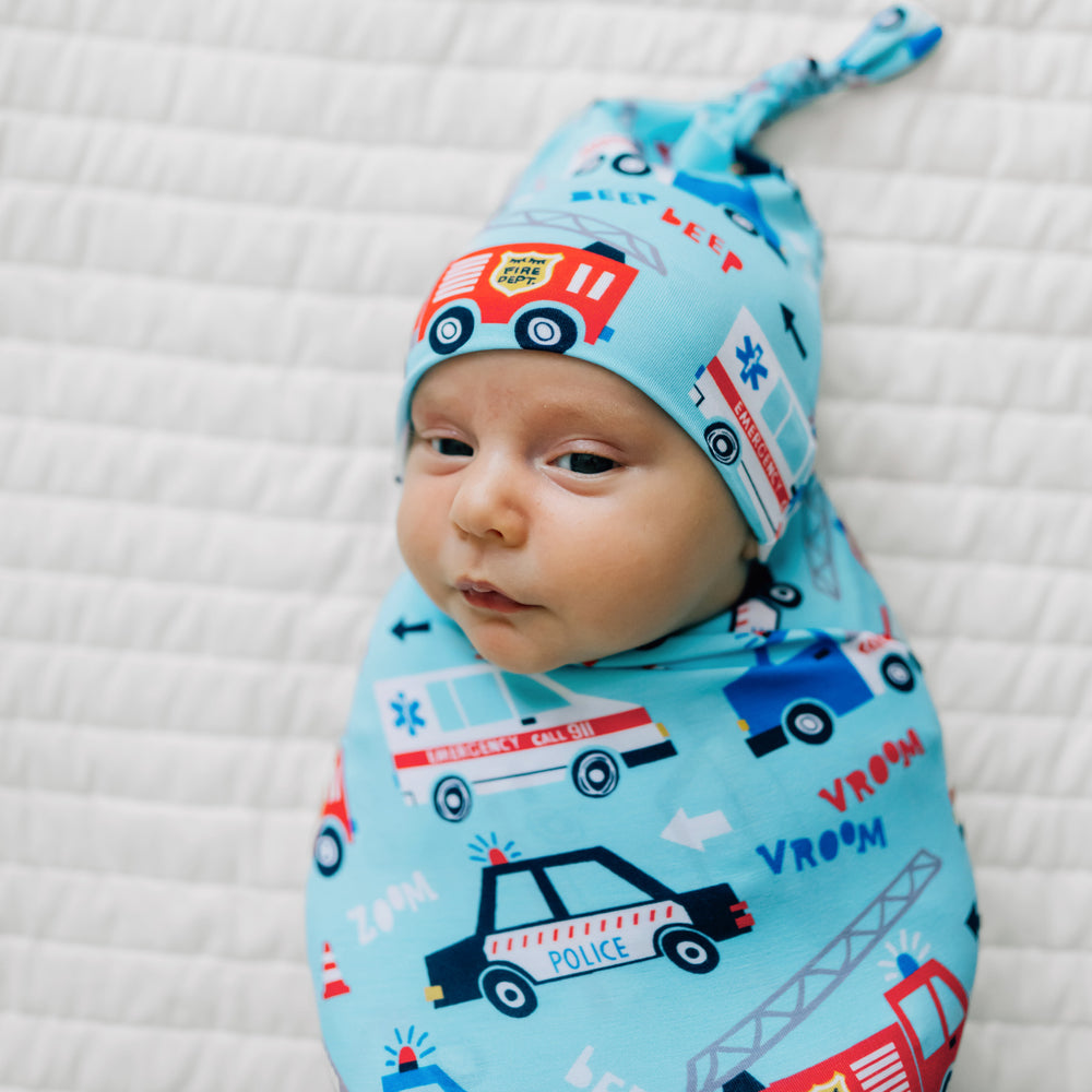 Close up image of a child laying on a bed swaddled in a To The Rescue swaddle and hat set