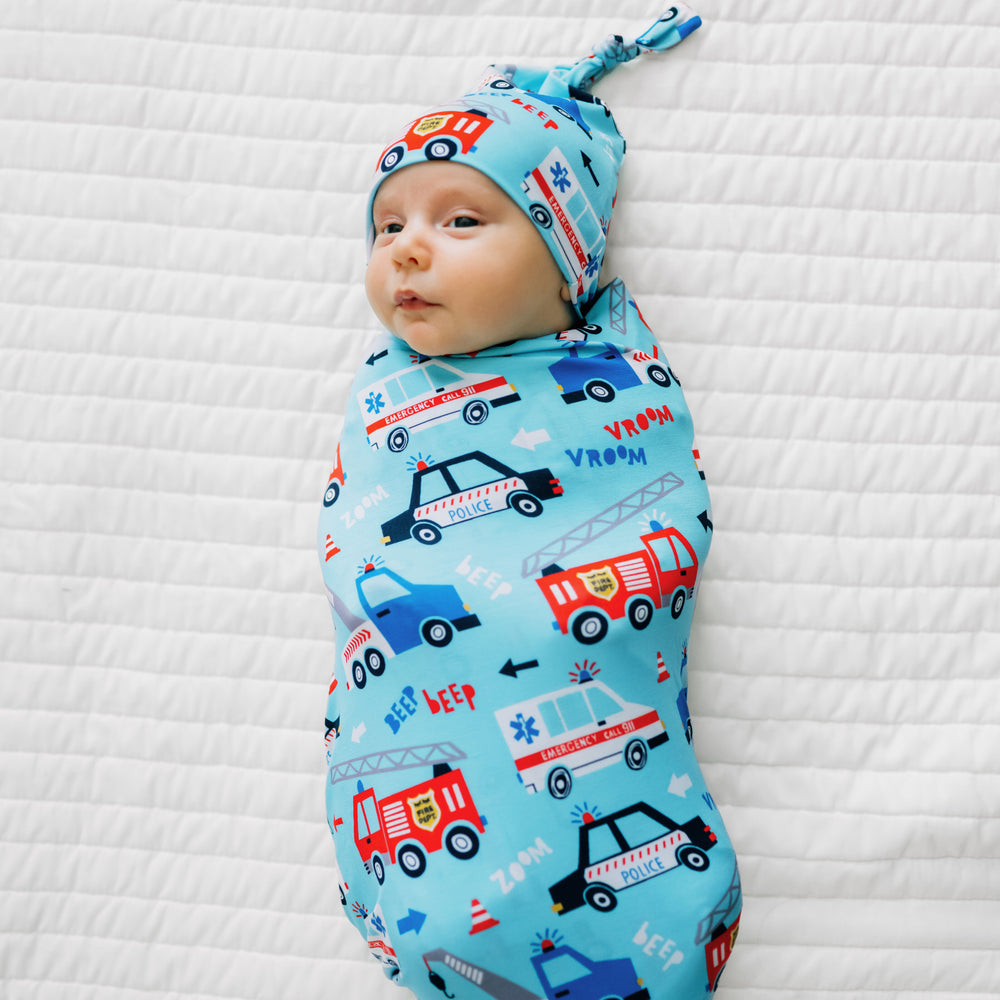 Child laying on a bed swaddled in a To The Rescue swaddle and hat set
