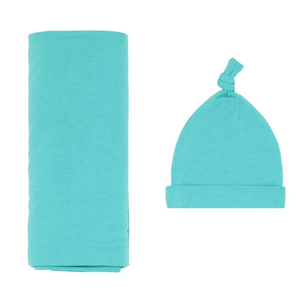 Flat lay image of a Glacier Turquoise swaddle and hat set