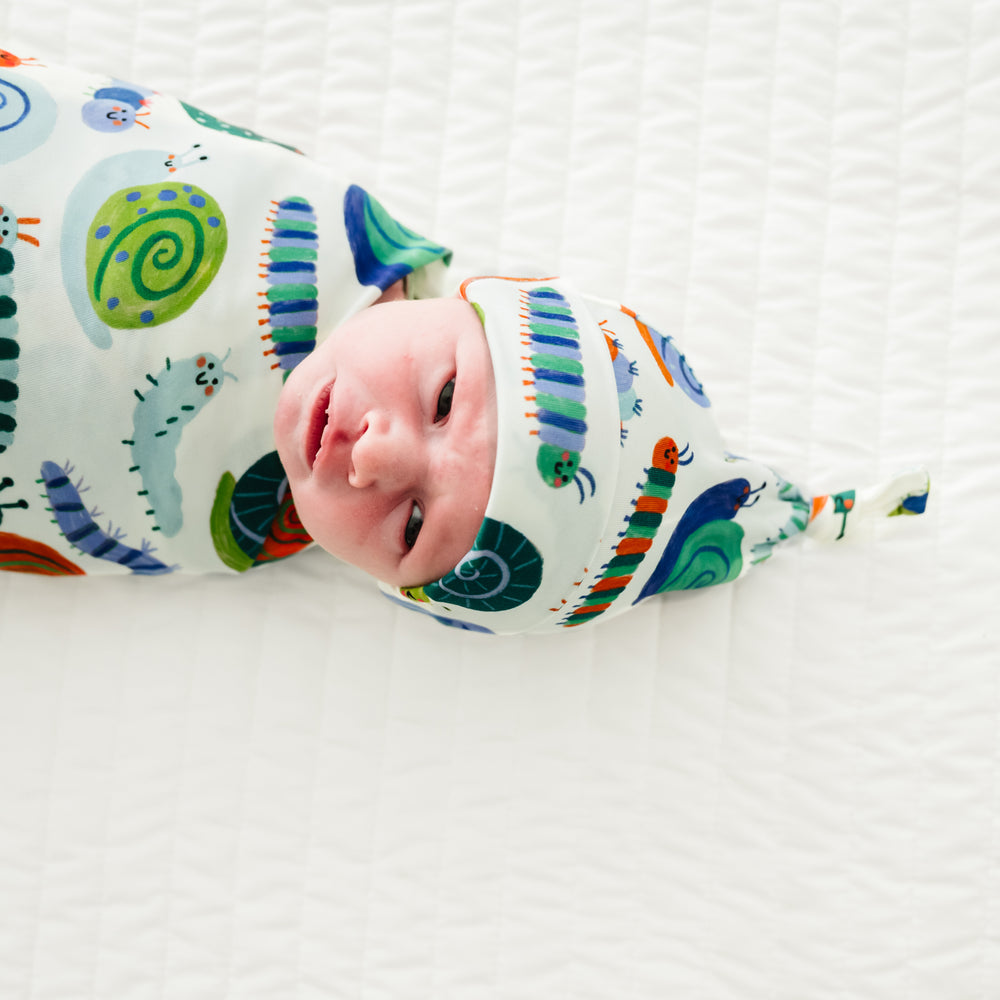 Close up image of an infant swaddled in an Inchin' Along swaddle & hat set