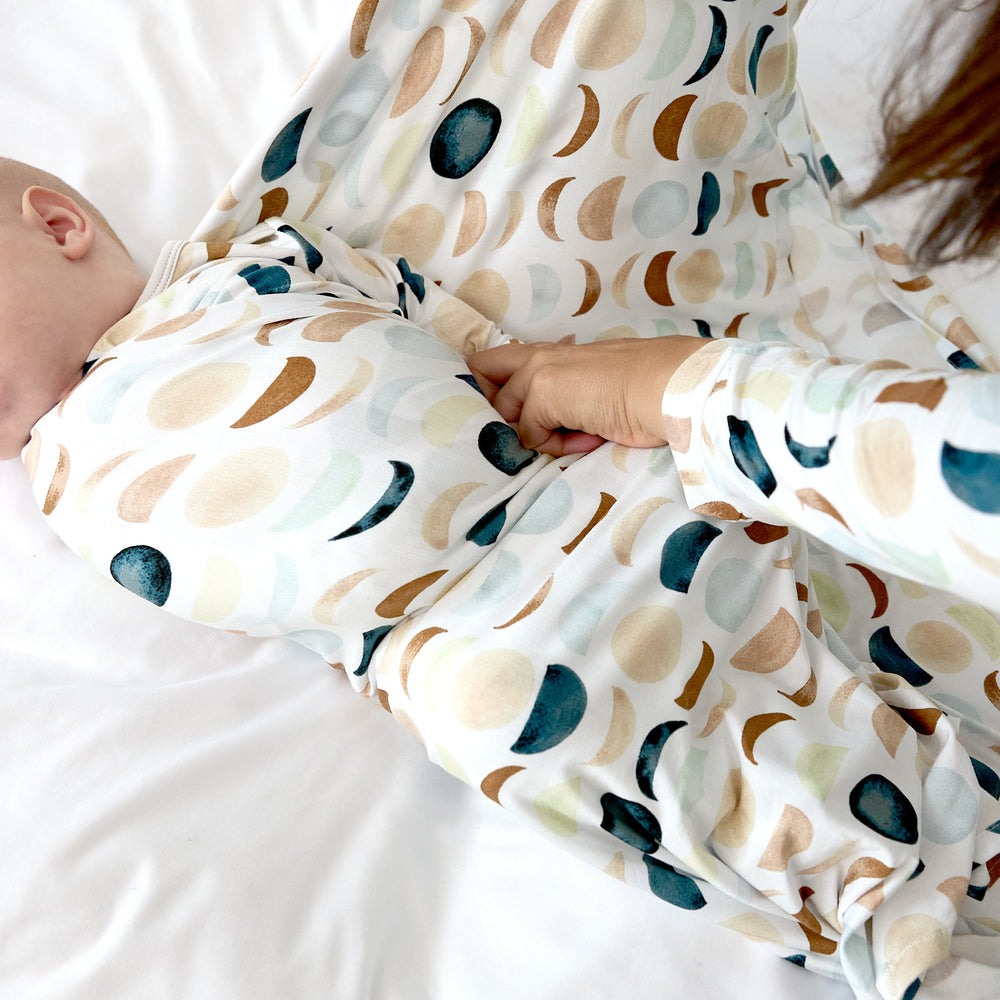 mom actively swaddling baby in luna neutral print