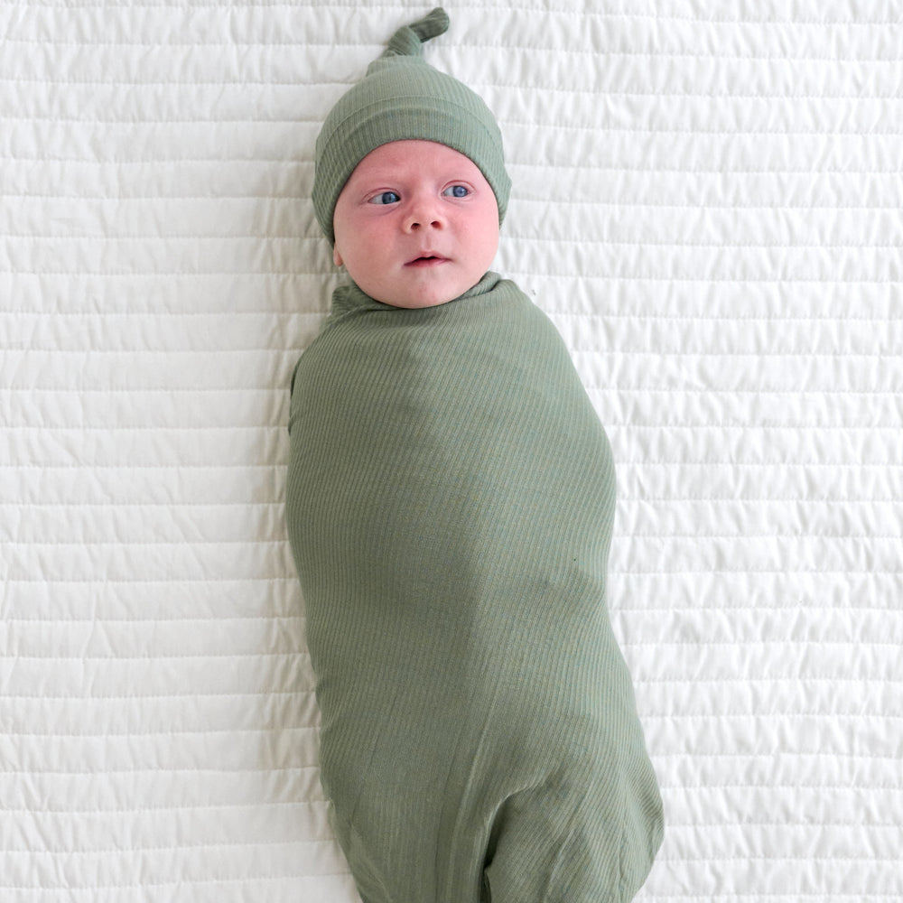 Top view image of baby laying down while wrapped in the Moss Ribbed Swaddle & Hat Set