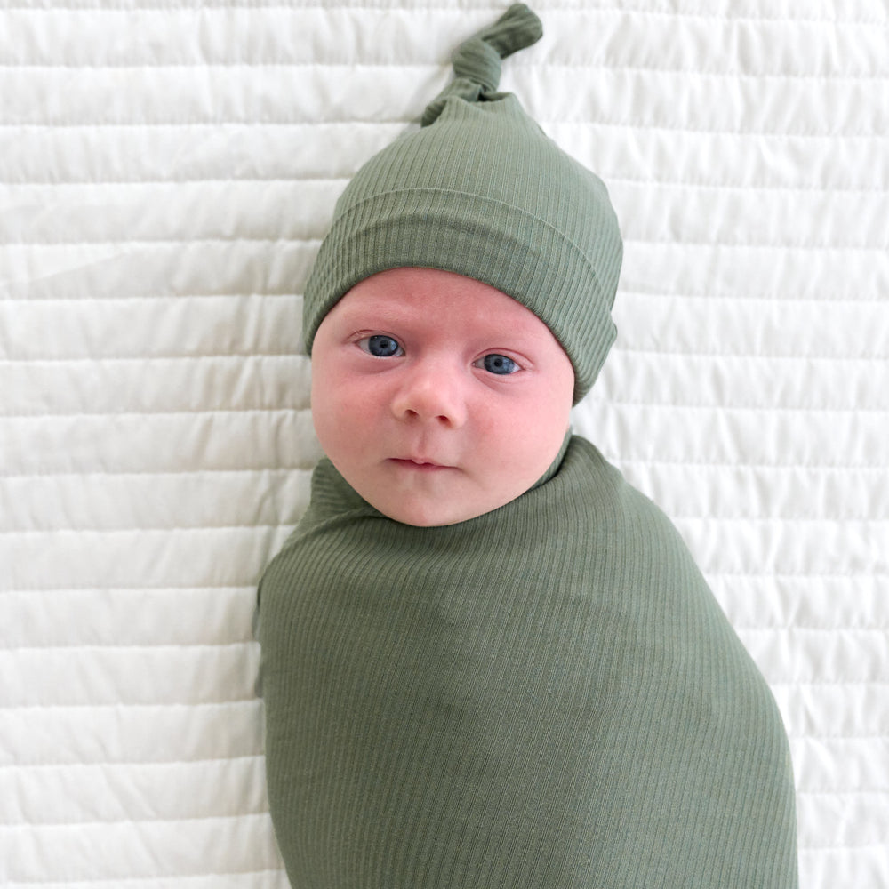 Top view close up image of baby laying down wearing the hat within the Moss Ribbed Swaddle & Hat Set