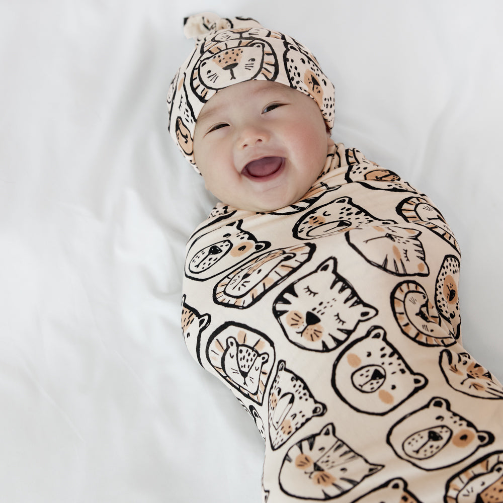 Close up image of a child swaddled in a Lions, Tigers, and Bears swaddle and hat shit