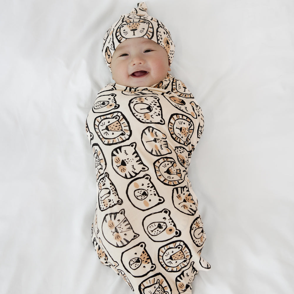 Image of a child swaddled in a Lions, Tigers, and Bears swaddle and hat shit