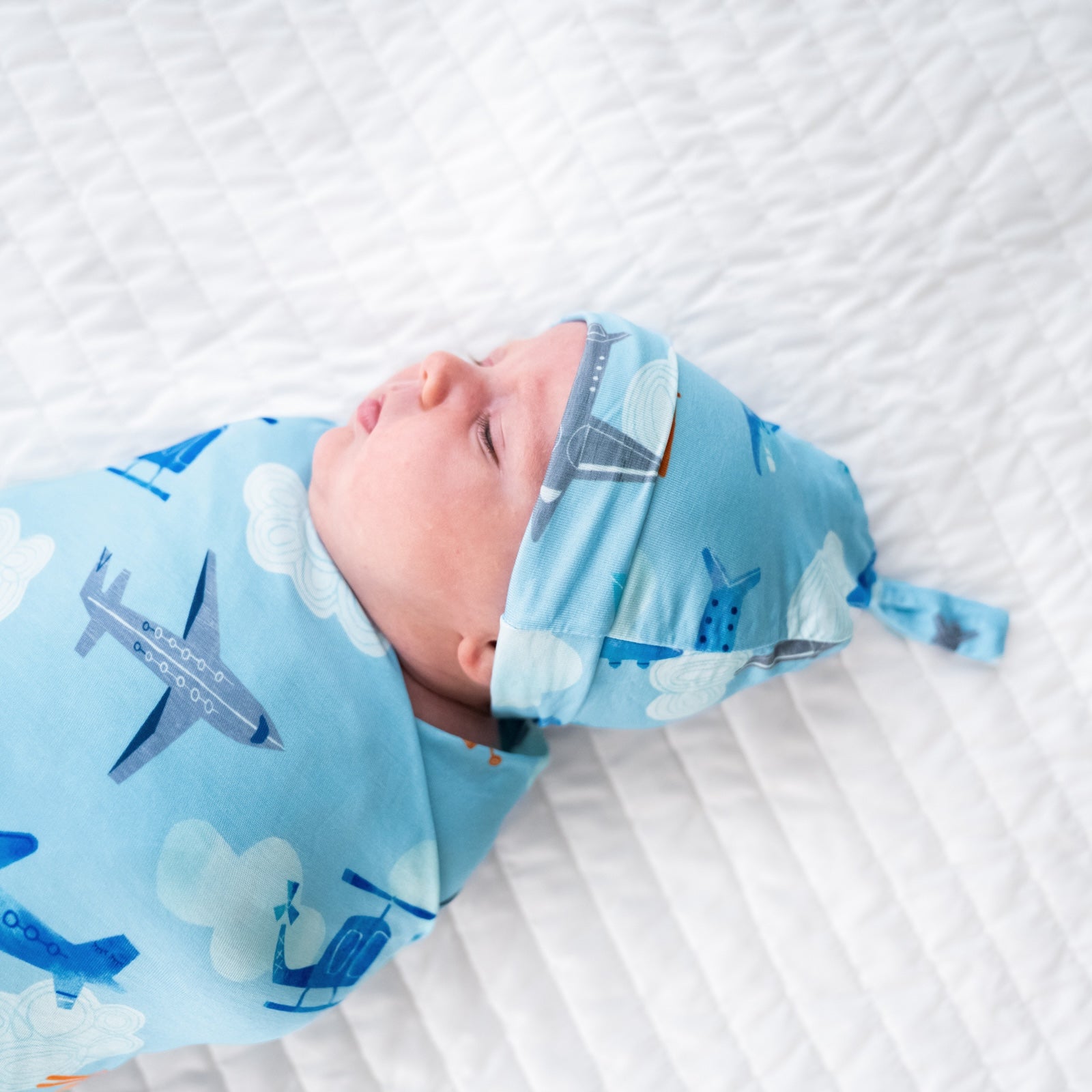 close up image of a child swaddled on a bed in a  Let's Fly swaddle and hat set