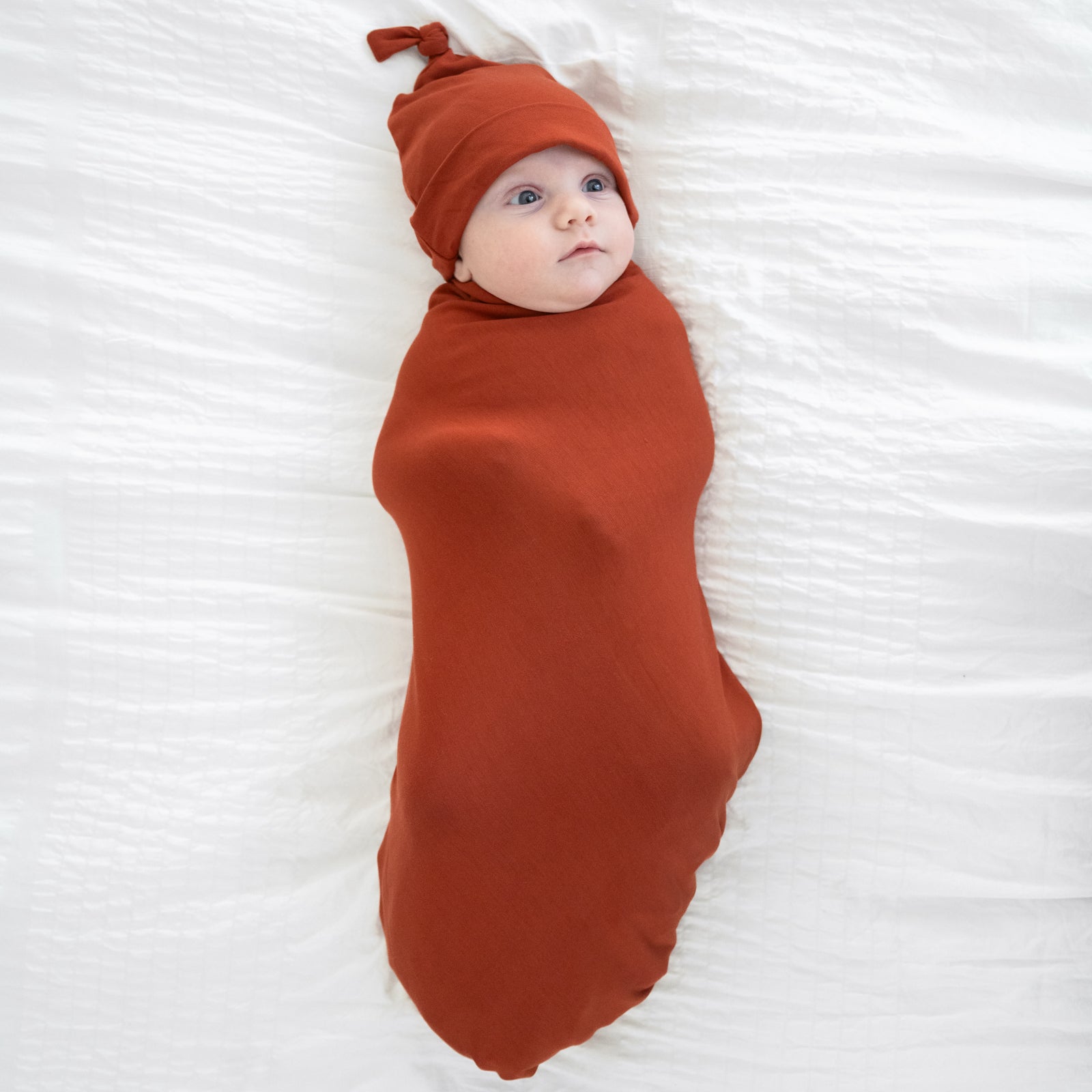 child swaddled in a Cozy Rust swaddle and hat set