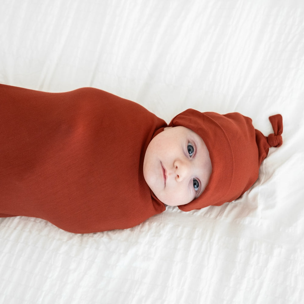 close up image of a child swaddled in a Cozy Rust swaddle and hat set