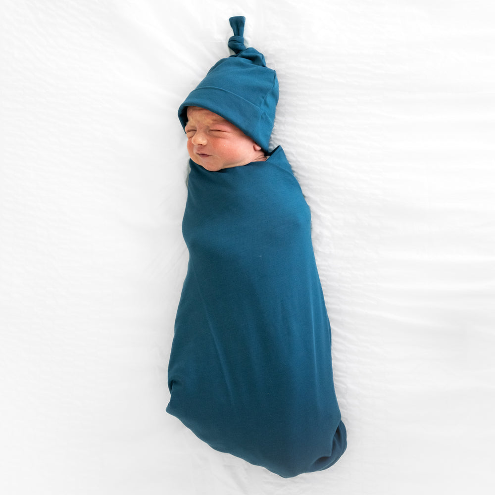 child swaddled in a Cozy Twilight Teal swaddle and hat set