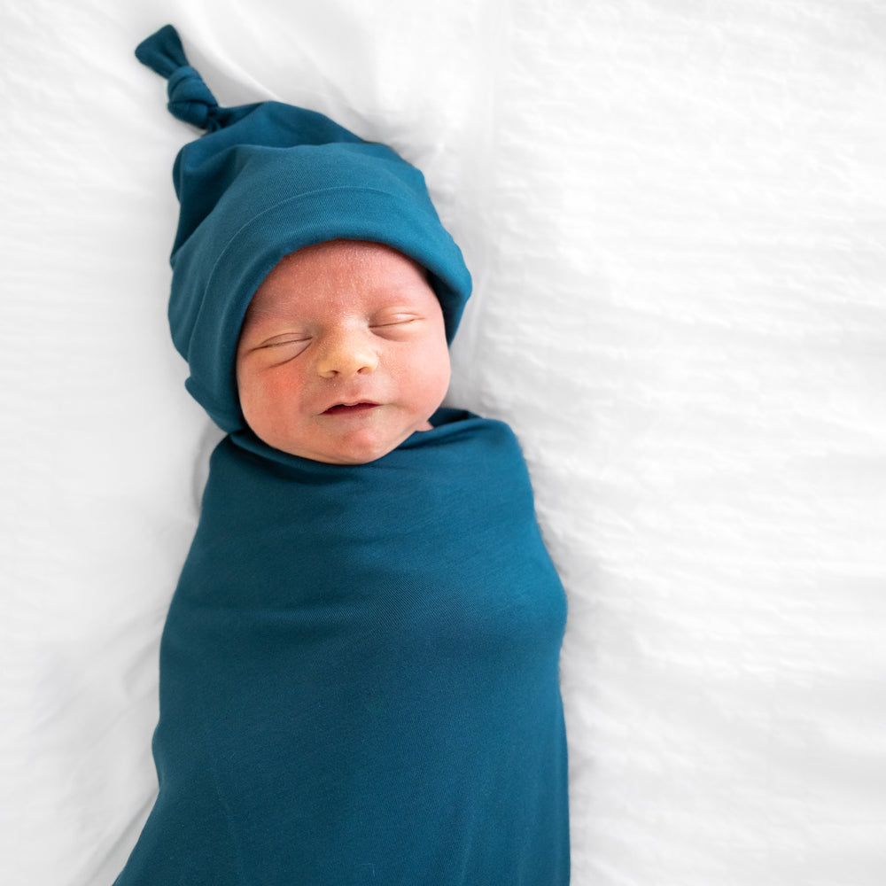 close up image of child swaddled in a Cozy Twilight Teal swaddle and hat set 