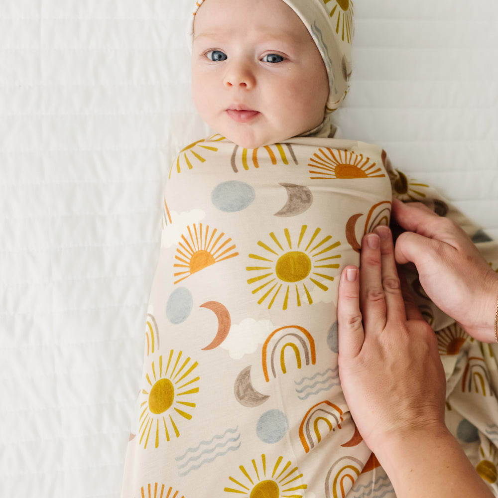 Image of a mother swaddling her child in a Desert Sunrise swaddle set