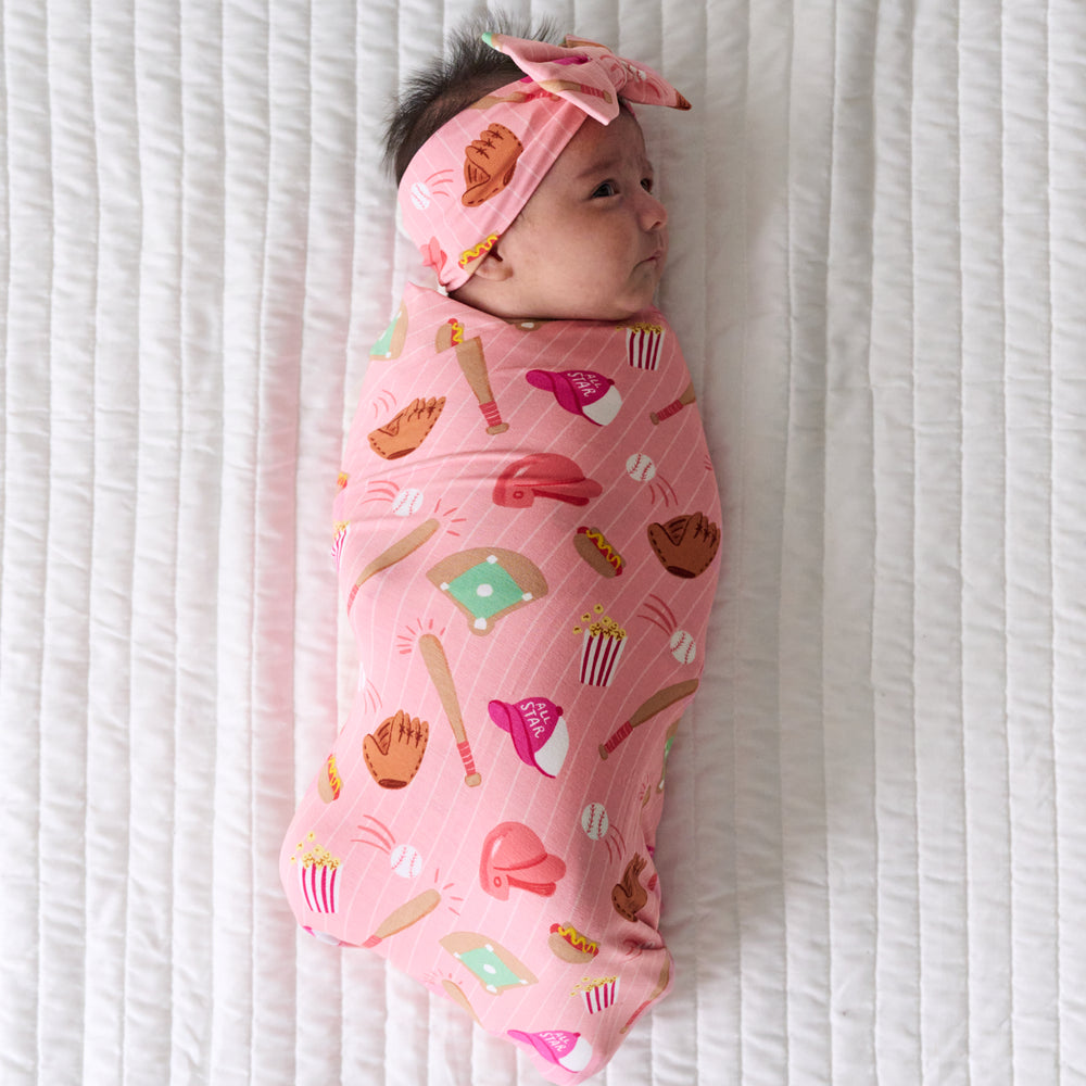 Child laying on a bed swaddled in a Pink All Stars swaddle and Luxe Bow Headband set