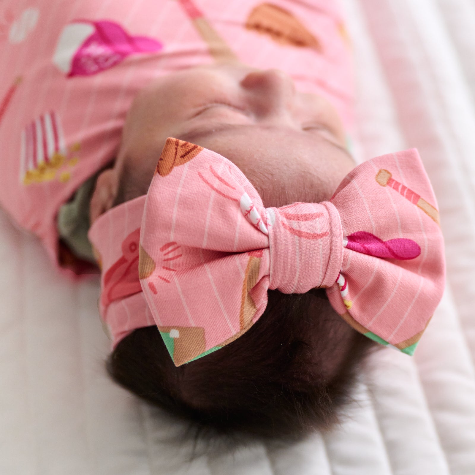 Close up image of a child swaddled in a Pink All Stars swaddle and luxe bow headband set showing off the luxe bow headband