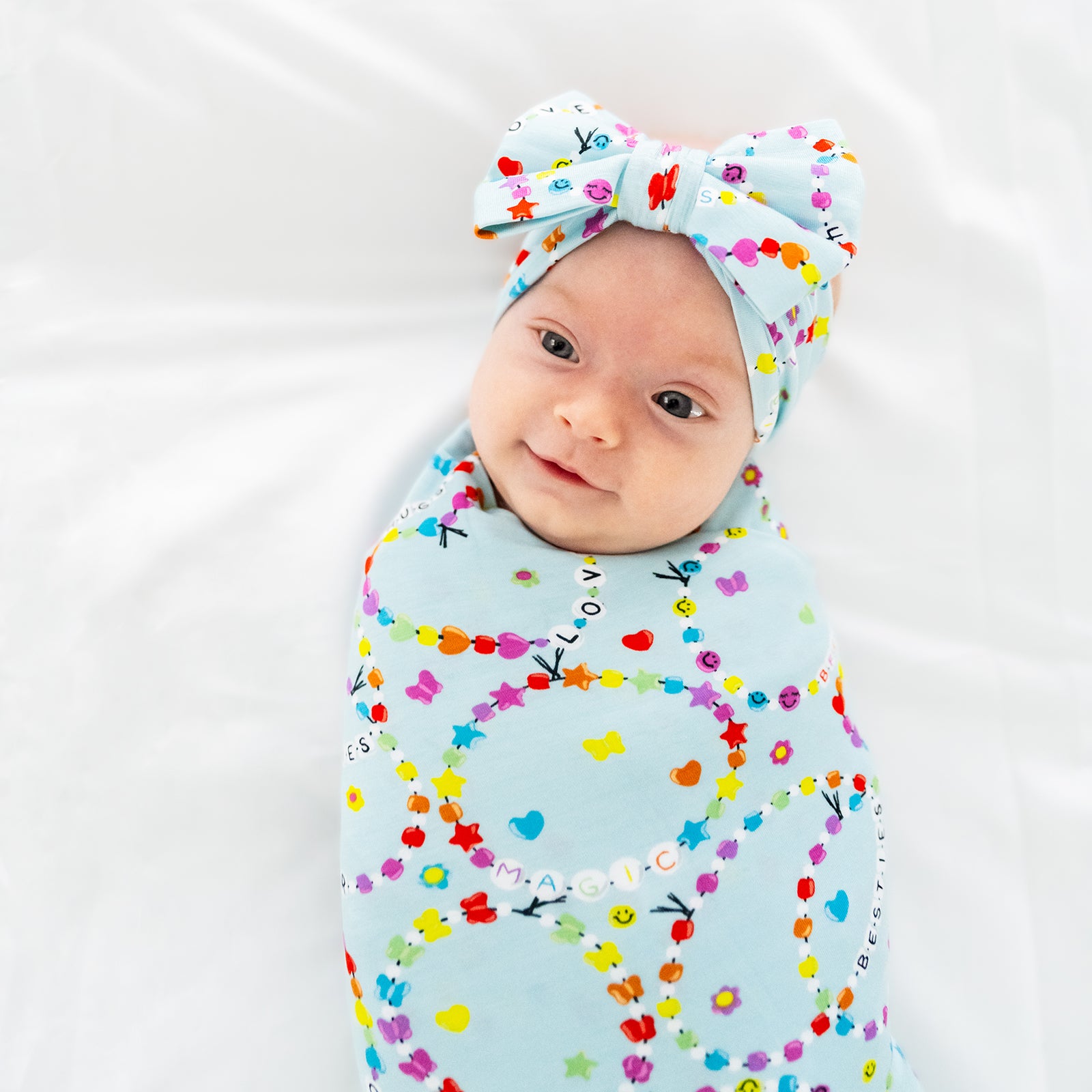 Alternative close up image of a child swaddled in a Friends Forever swaddle and bow set on a bed